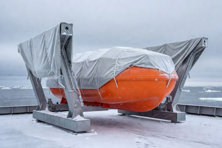 Totally enclosed orange polar lifeboat suspended on trace-heated gravity davits with protective ice canvas covers